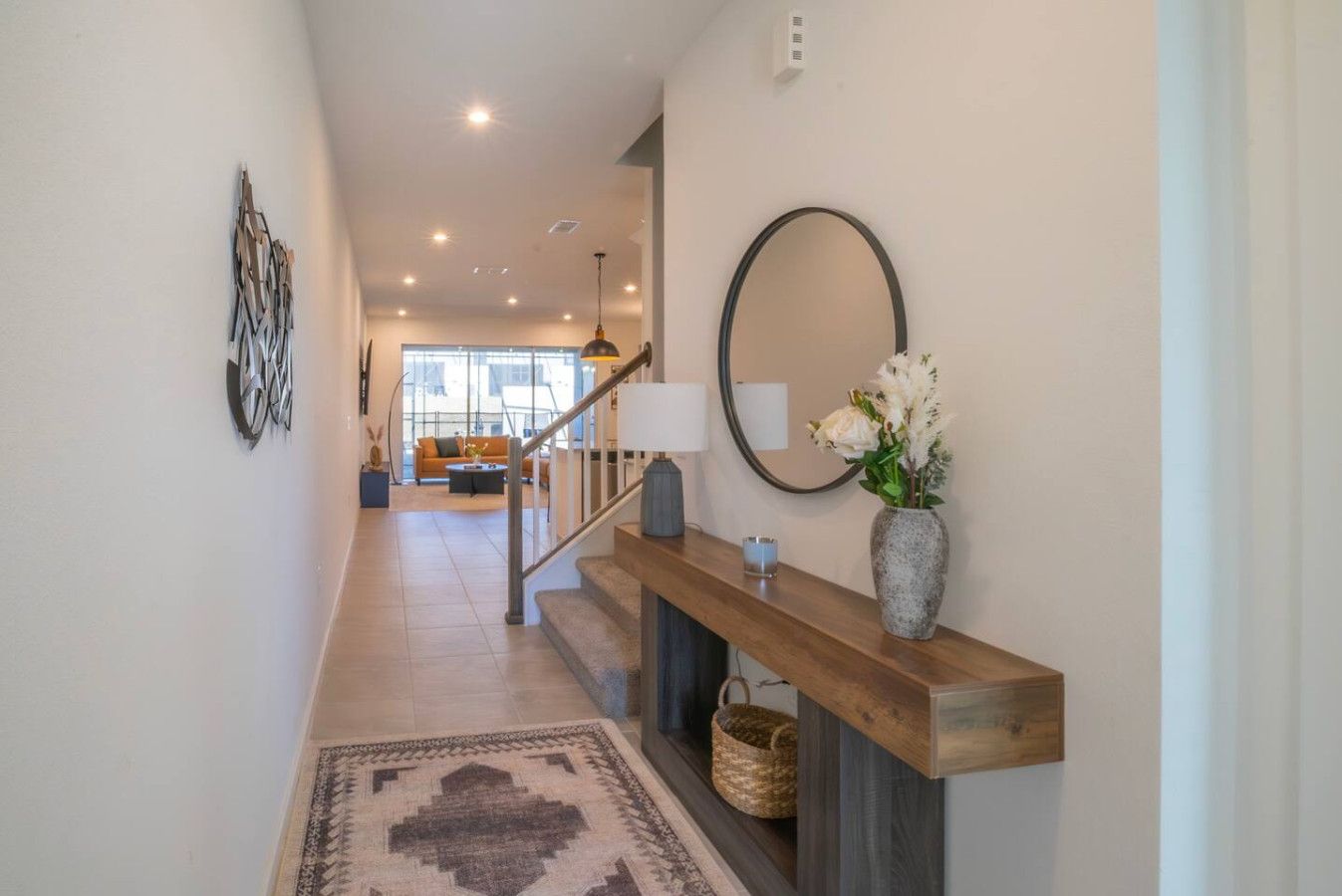 A modern interior with a wooden staircase, a mirror, a vase with flowers, and a view into a living area.