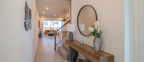 Ein modernes Interieur mit einer Holztreppe, einem Spiegel, einer Vase mit Blumen und Blick in einen Wohnbereich.