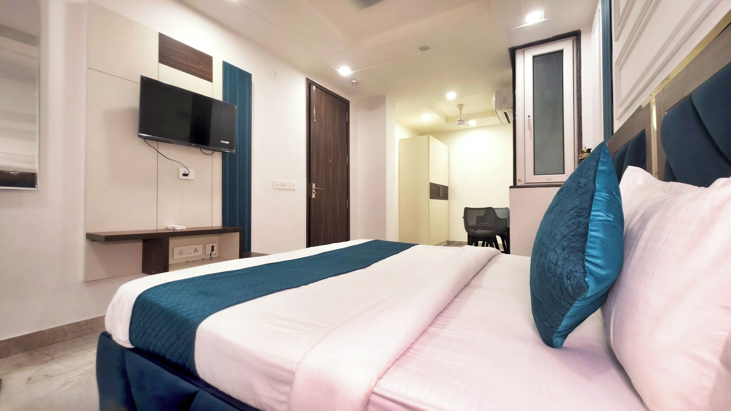 Quarto de hotel com cama, televisão fixada na parede, escrivaninha e cadeira.