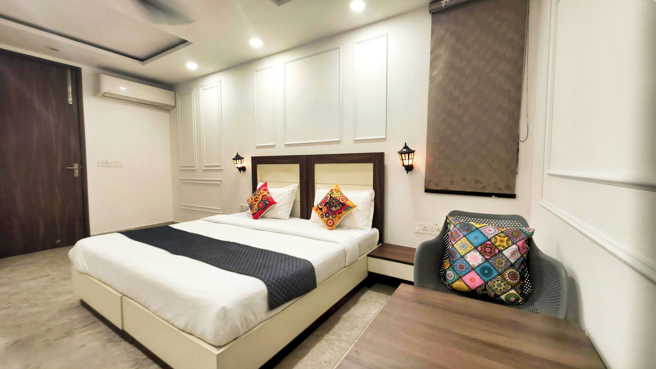 Habitación de hotel con una cama grande, un escritorio y una silla. Cuenta con lámparas de pared y un equipo de aire acondicionado.