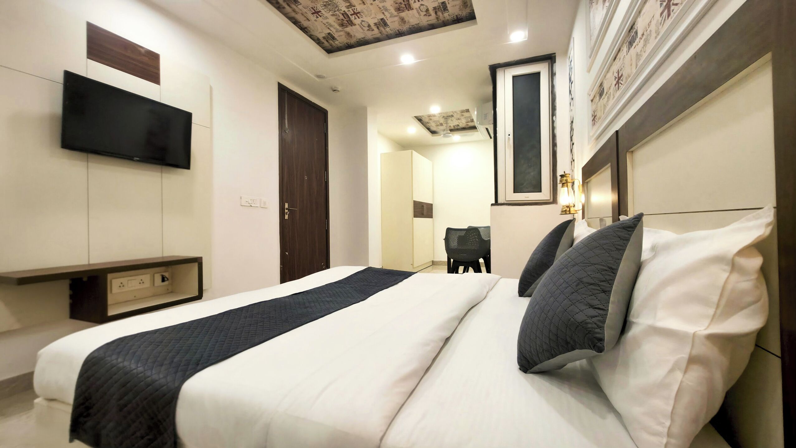 Una habitación de hotel moderna con una cama grande, un televisor de pantalla plana montado en la pared, un escritorio con una silla y un techo con un diseño decorativo.