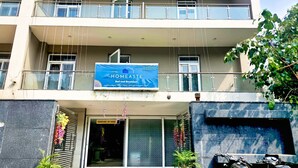 Un hotel con un letrero que anuncia "HOMEASTE Bed and Breakfast" y un número de contacto. Hay escalones que conducen a la entrada, plantas en macetas y una motocicleta estacionada afuera.