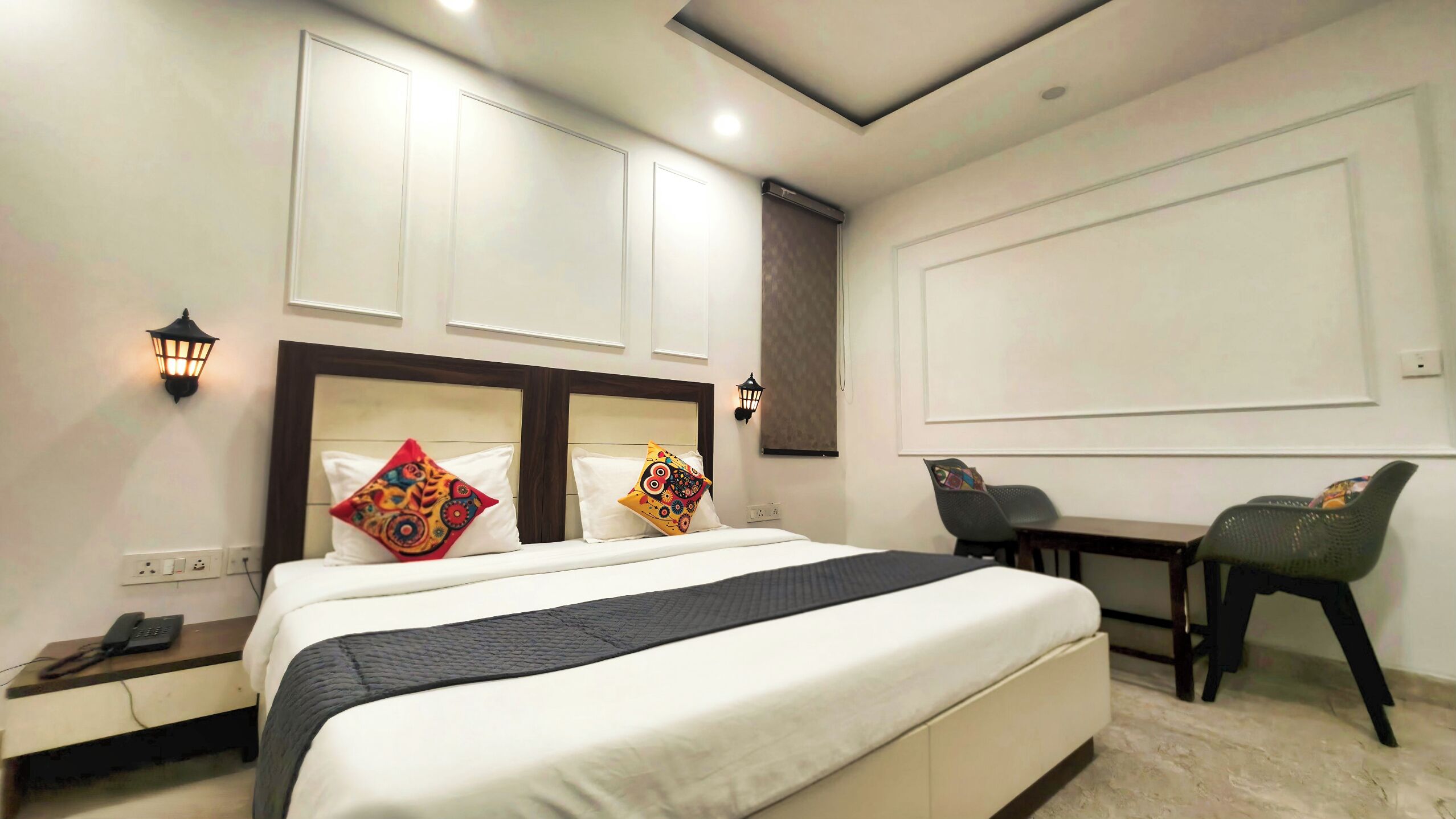 A hotel room with a large bed, two bedside tables, a desk, and two chairs.