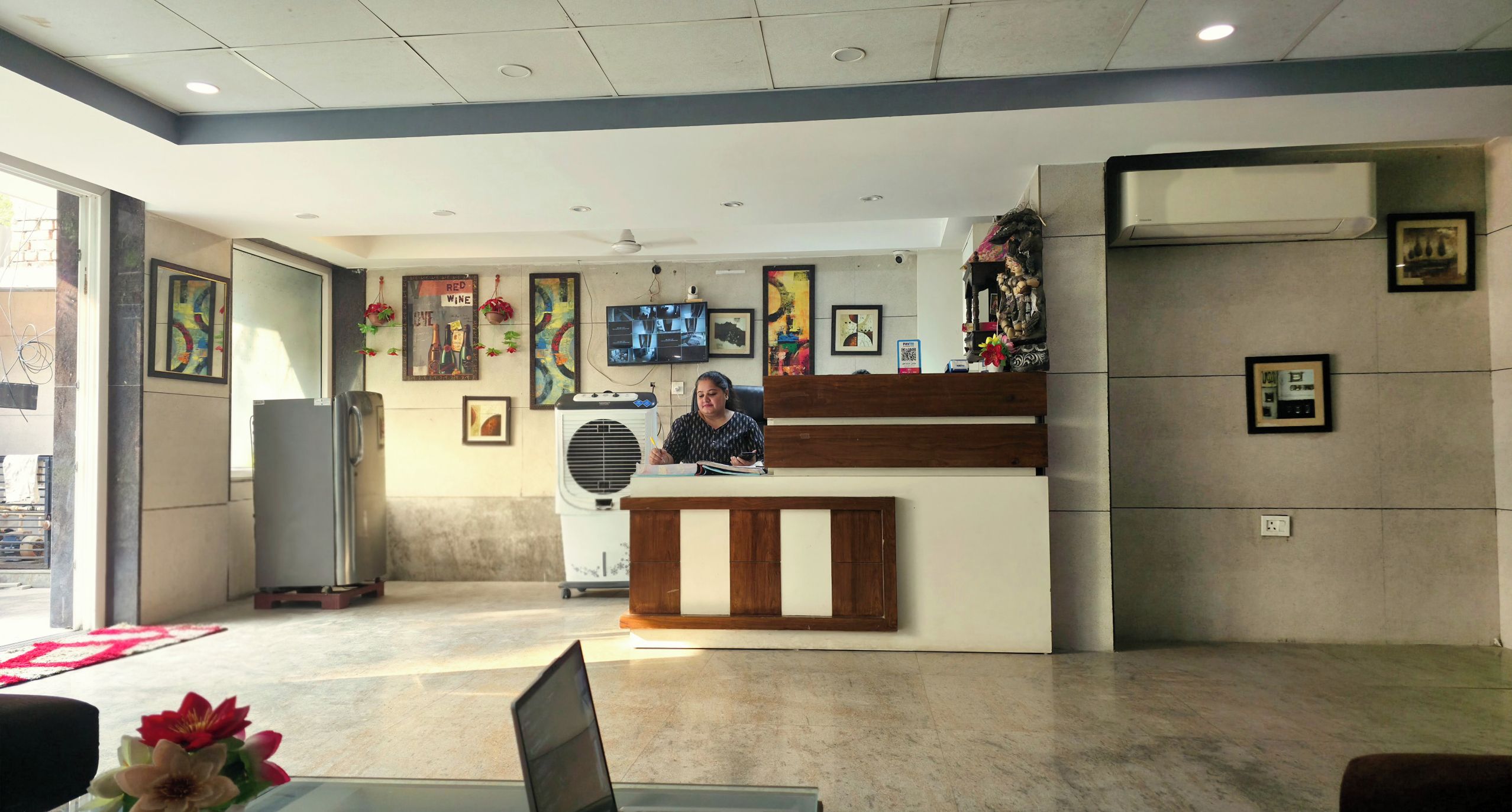 Un espace d’accueil comprenant un comptoir de réception, un bureau, un grand appareil de climatisation et divers tableaux encadrés accrochés aux murs.