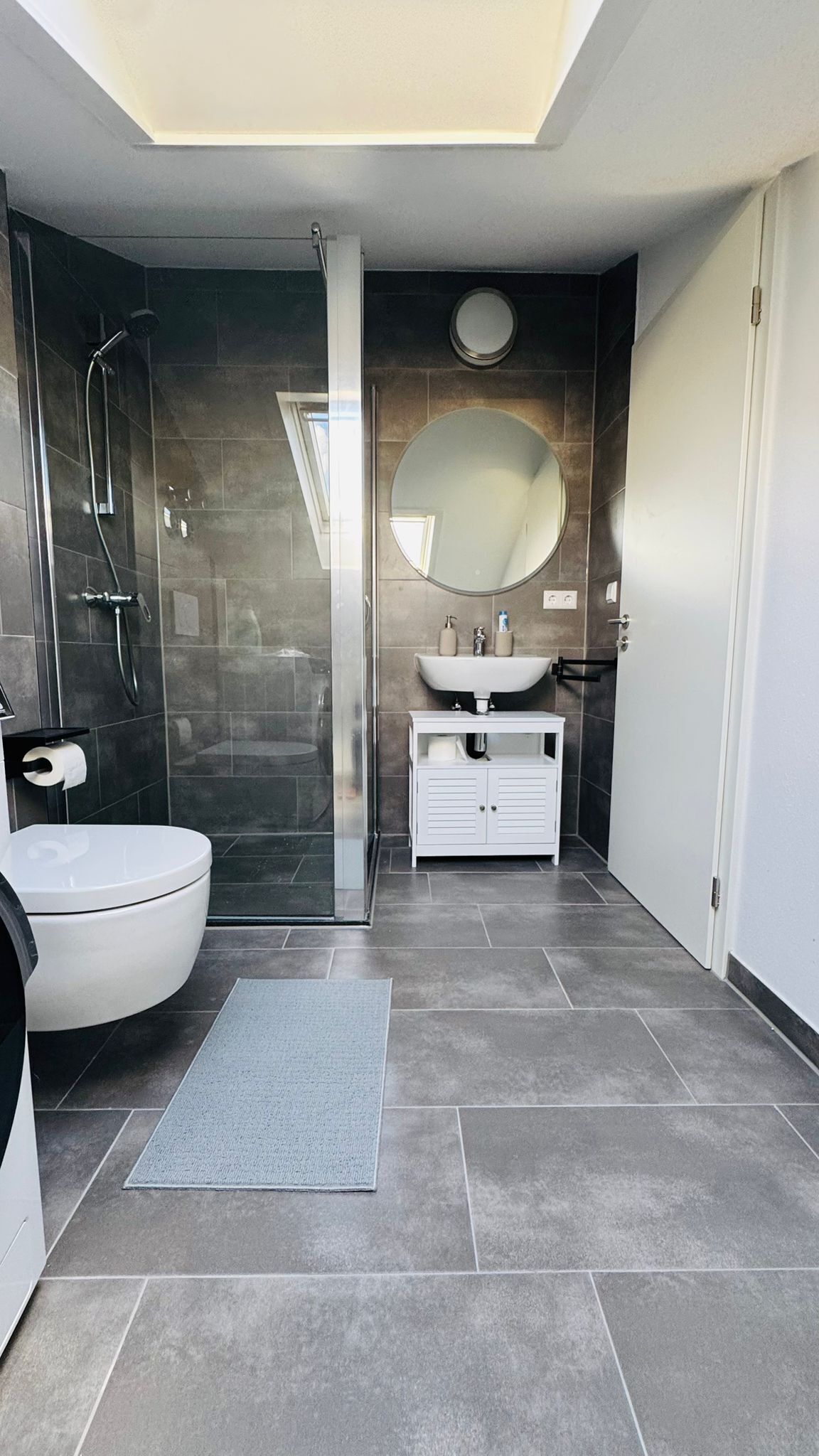 A modern bathroom with a glass-enclosed shower, a white toilet, a sink with a mirror, and a white vanity.