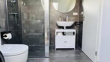 A modern bathroom with a glass-enclosed shower, a white toilet, a sink with a mirror, and a white vanity.