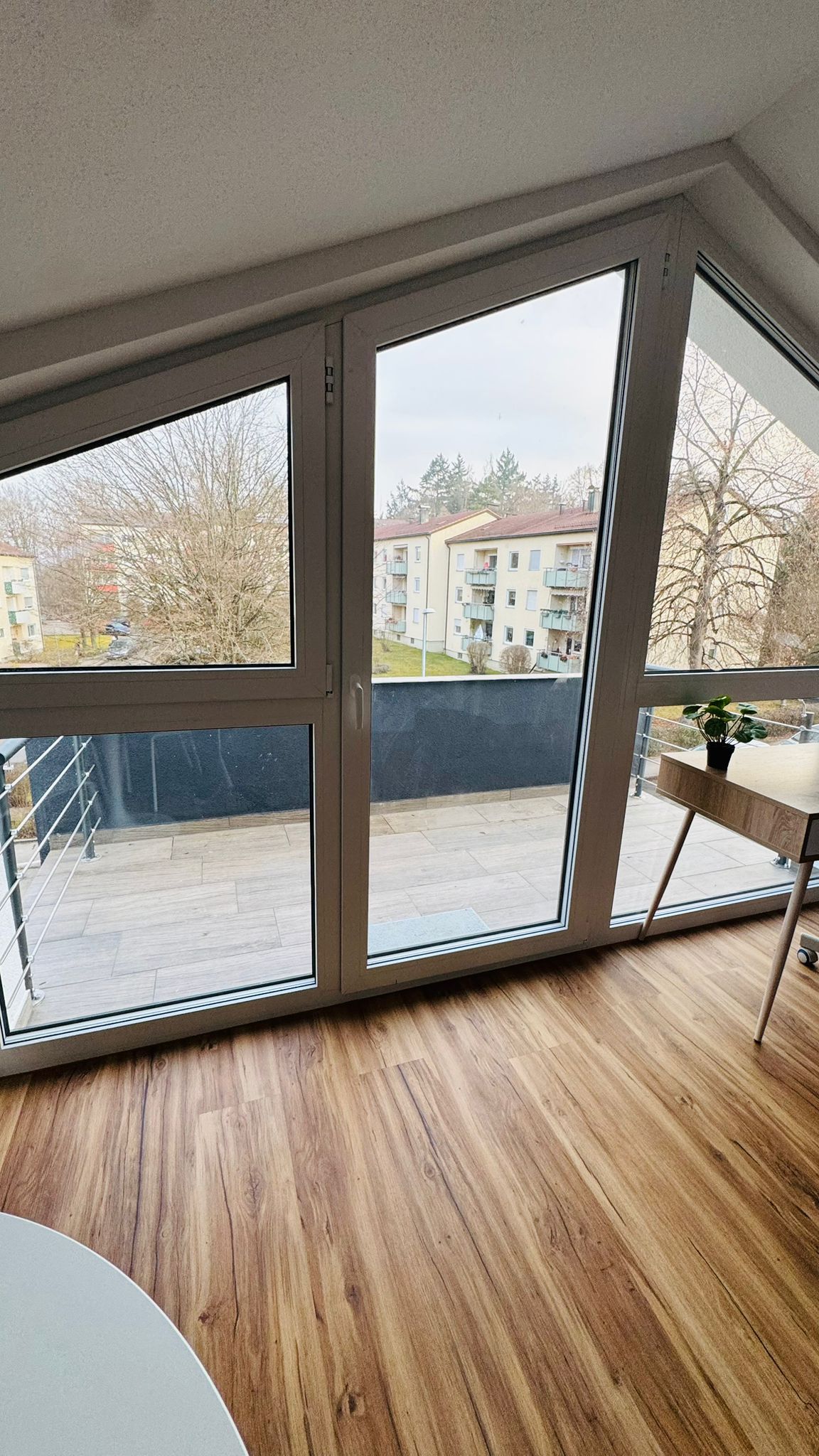 A room with large floor-to-ceiling windows, a wooden floor, and a small table with a potted plant.