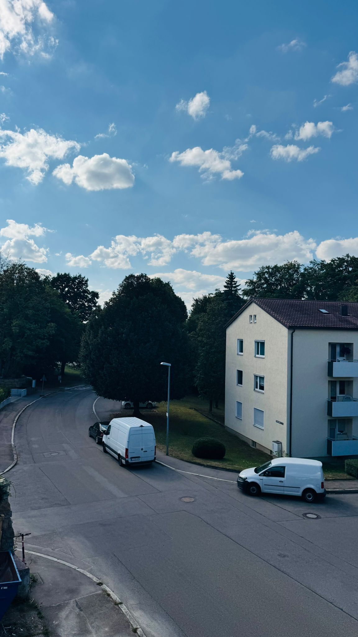 A residential street with two white vans parked on the side, a clear blue sky, and a building with a flat roof and multiple windows.