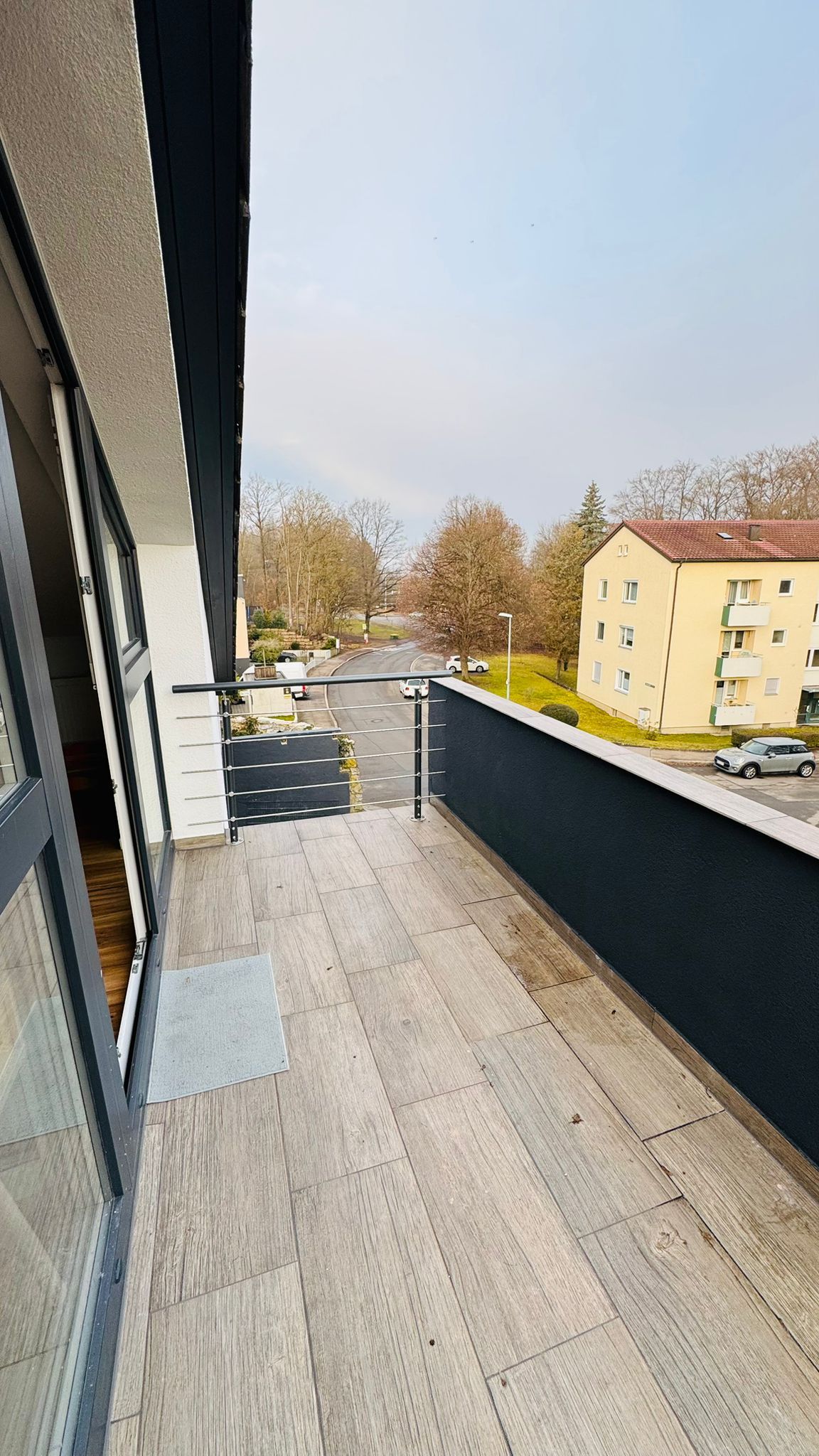 Ein Balkon mit Blick auf einen Parkplatz und ein Gebäude gegenüber.