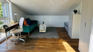 En rymlig loftvåning med trägolv, en grön soffa, ett skrivbord med stol och ett vitt skåp.