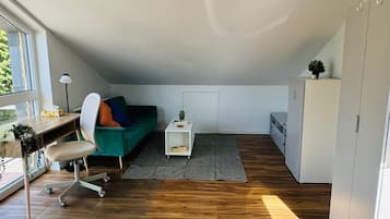 Ein geräumiger Lofts mit Holzboden, einem grünen Sofa, einem Schreibtisch mit Stuhl und einem weißen Schrank.