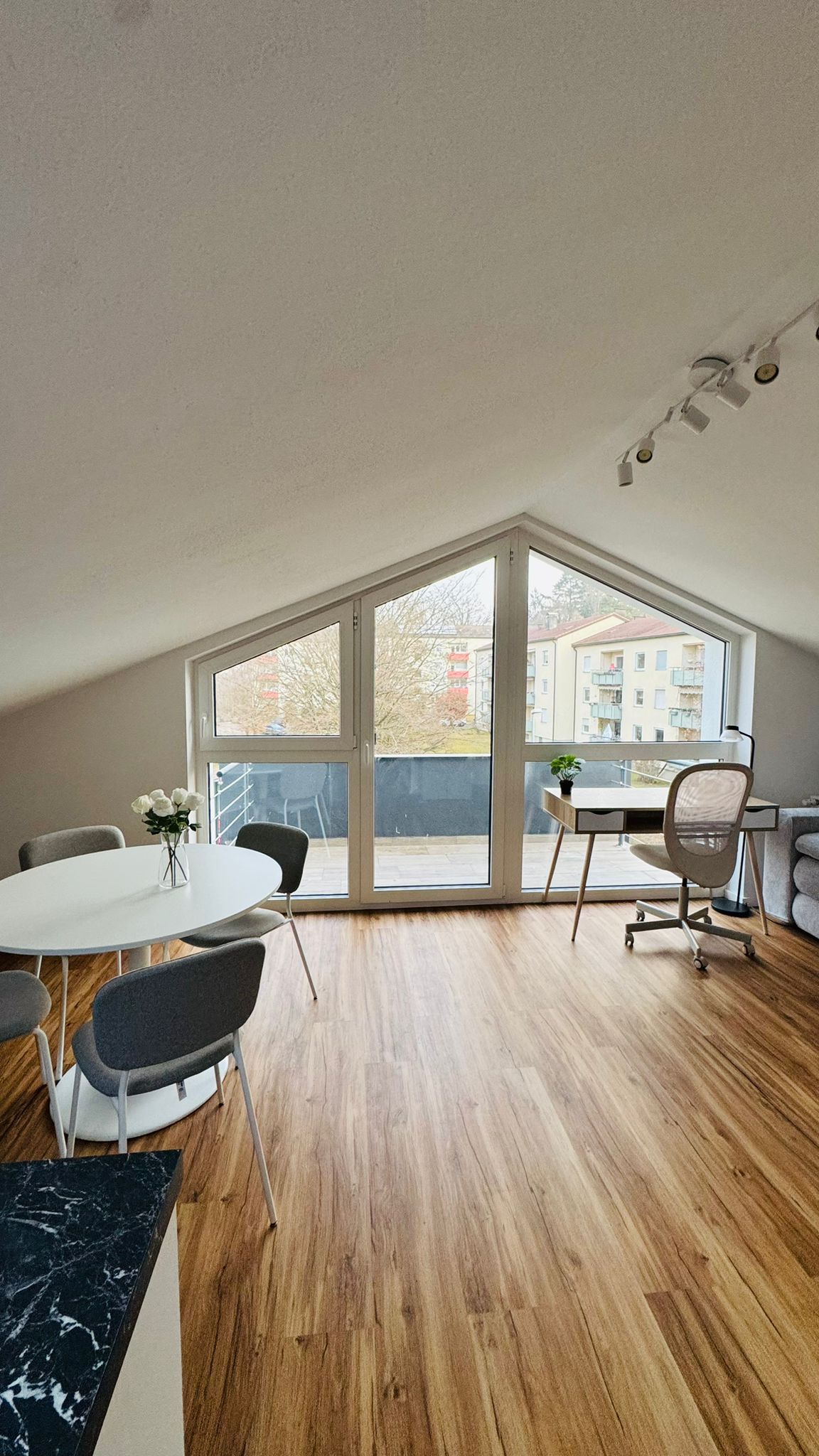 Une pièce spacieuse avec une grande fenêtre, une table à manger ronde et un bureau avec une chaise.