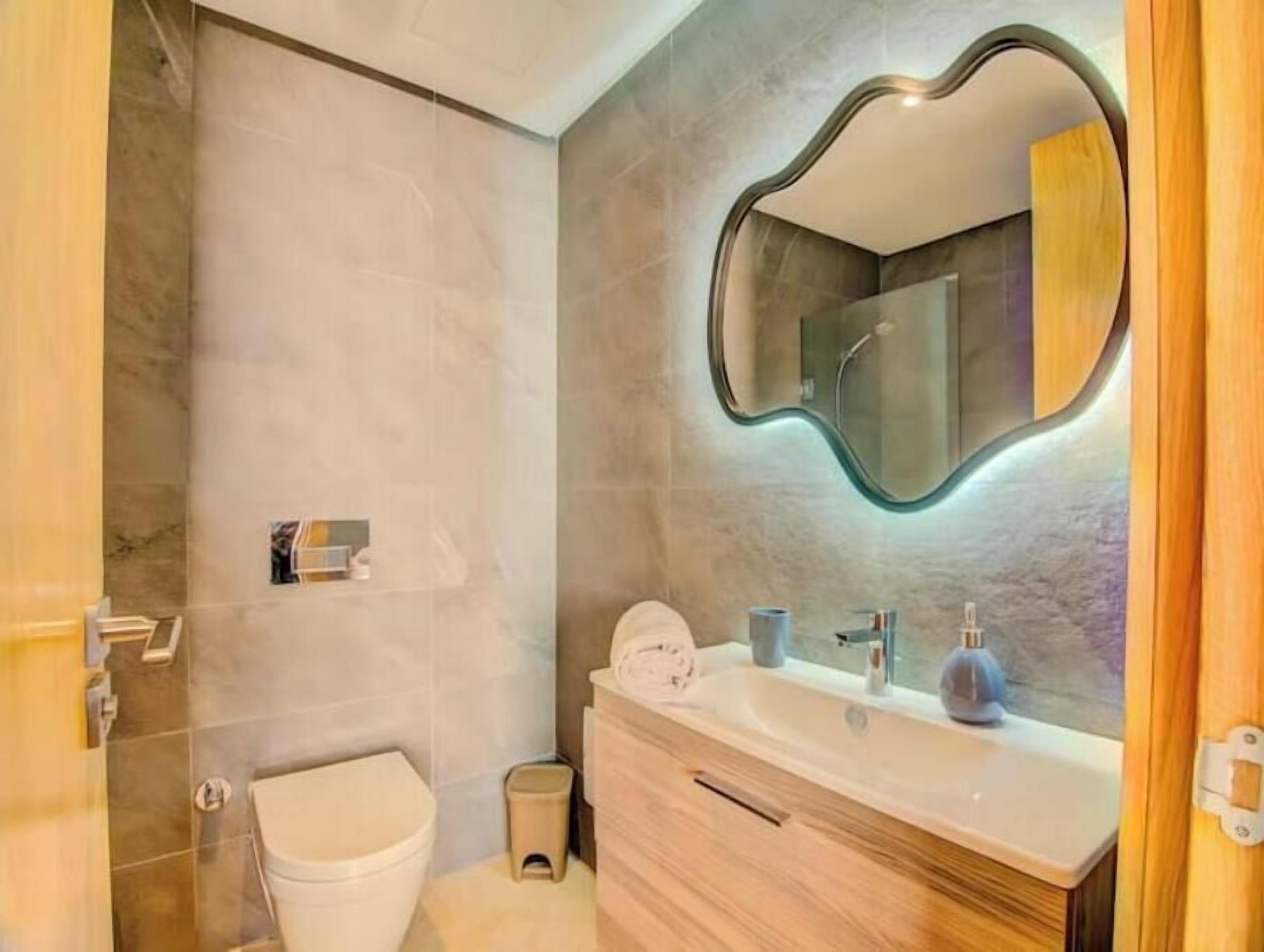 A modern bathroom with a toilet, vanity, and a mirror with a unique frame.