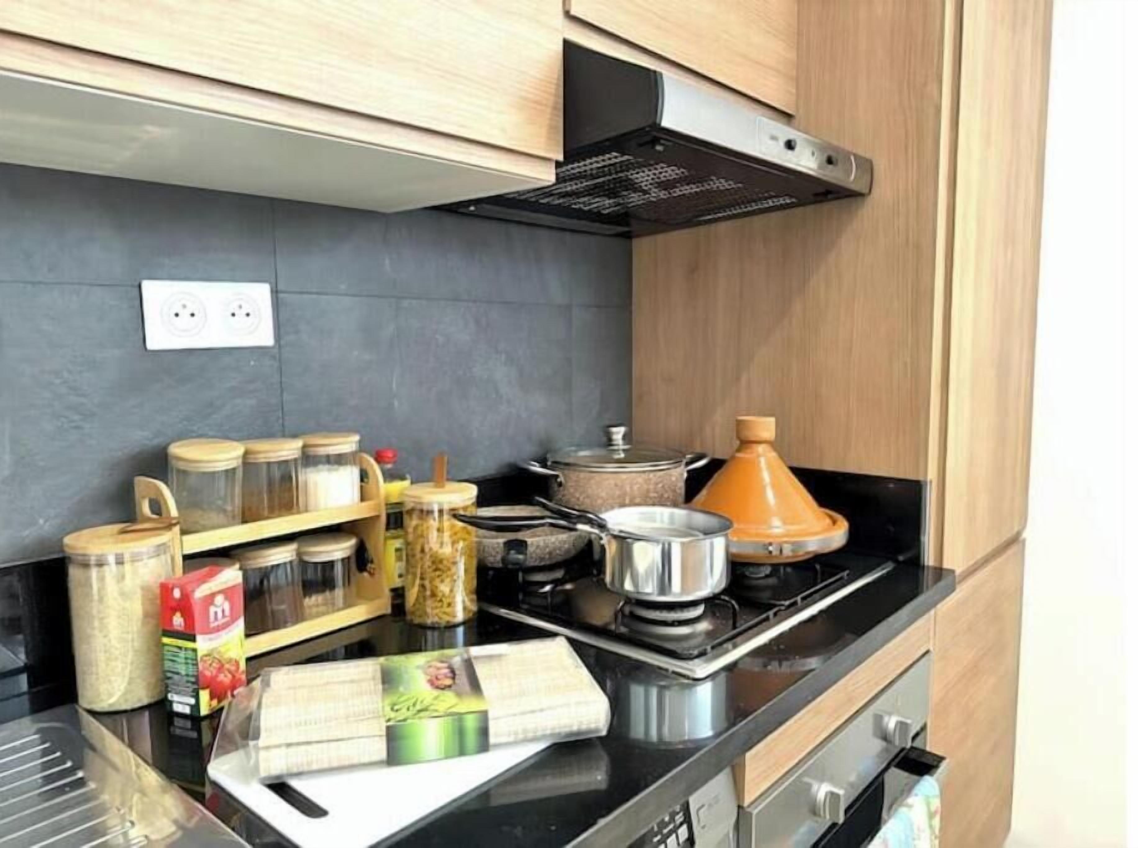 A kitchen with wooden cabinets, a black countertop, and various kitchen items including jars, a pot, and a stove.