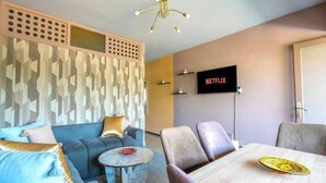 A modern living room with a sofa, a coffee table, and a dining table. A flat-screen TV mounted on the wall displays the Netflix logo. - Cosy calm Studio in the hyper center (Agadir)