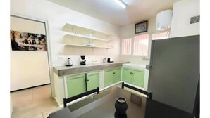 Een kleine keuken met groene kastjes, een zwart aanrecht en een koelkast.