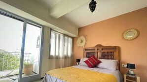 Een slaapkamer met een bed, nachtkastje, spiegel en een balkondeur.