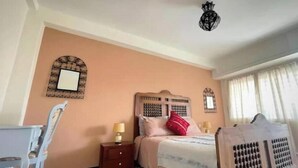 Een slaapkamer met een bed, nachtkastje, stoel en decoratieve wandversiering.