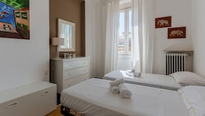 Een hotelkamer met twee bedden, een kaptafel, een schilderij en een raam met gordijnen.