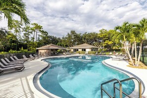 A swimming pool with lounge chairs and a covered area, surrounded by trees and a building. - Private Pool, Firepit, Game Room Mins to Beaches + Community Amenities Casa Solara by Avantstay (Naples)
