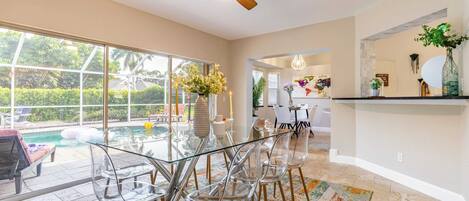 A spacious room with a glass dining table, clear chairs, a ceiling fan, and a view of a swimming pool.