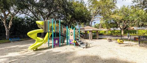 A playground with a yellow slide, climbing structures, and a covered seating area.