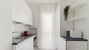 Een moderne keuken met witte kastjes, een roestvrijstalen spoelbak, een magnetron en een rode waterkoker.