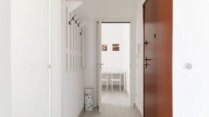 Een hal met een witte deur, een prullenbak en een witte tafel met stoelen.
