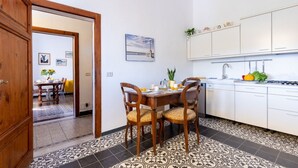 Une cuisine avec des meubles blancs, une table à manger avec des chaises et un sol carrelé.