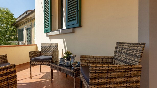 Un balcon agrémenté de meubles en osier, une table avec un service à thé, et un bâtiment aux volets verts.