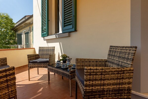 A balcony with wicker furniture, a table with tea set, and a building with green shutters.