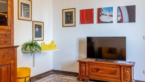 Un salon avec un téléviseur, un meuble en bois, un fauteuil jaune et des tableaux accrochés au mur.