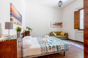 Ein Schlafzimmer mit einem Bett, einem grünen Sofa, einem Holzkabinett, einer Topfpflanze und einem Bild an der Wand.