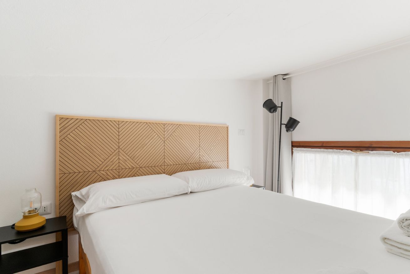 A hotel room with a bed, a nightstand, a lamp, and a window with curtains.