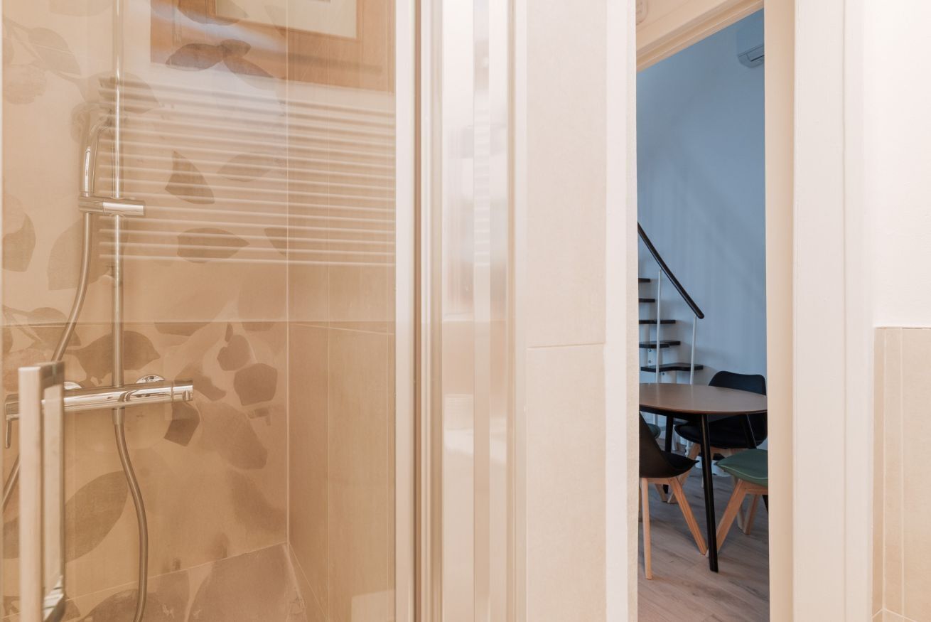 Een moderne badkamer met een glazen douchecabine, een zichtbare douchekop en een betegelde vloer.