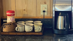 Uma cozinha com uma cafeteira, um recipiente com café e vários copos em um suporte.