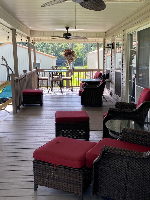 A covered outdoor deck with wicker furniture, a ceiling fan, and a view of the backyard.
