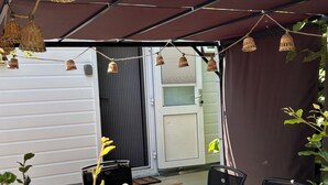 A covered patio area with a sliding door, a black grill, and a wooden bench.