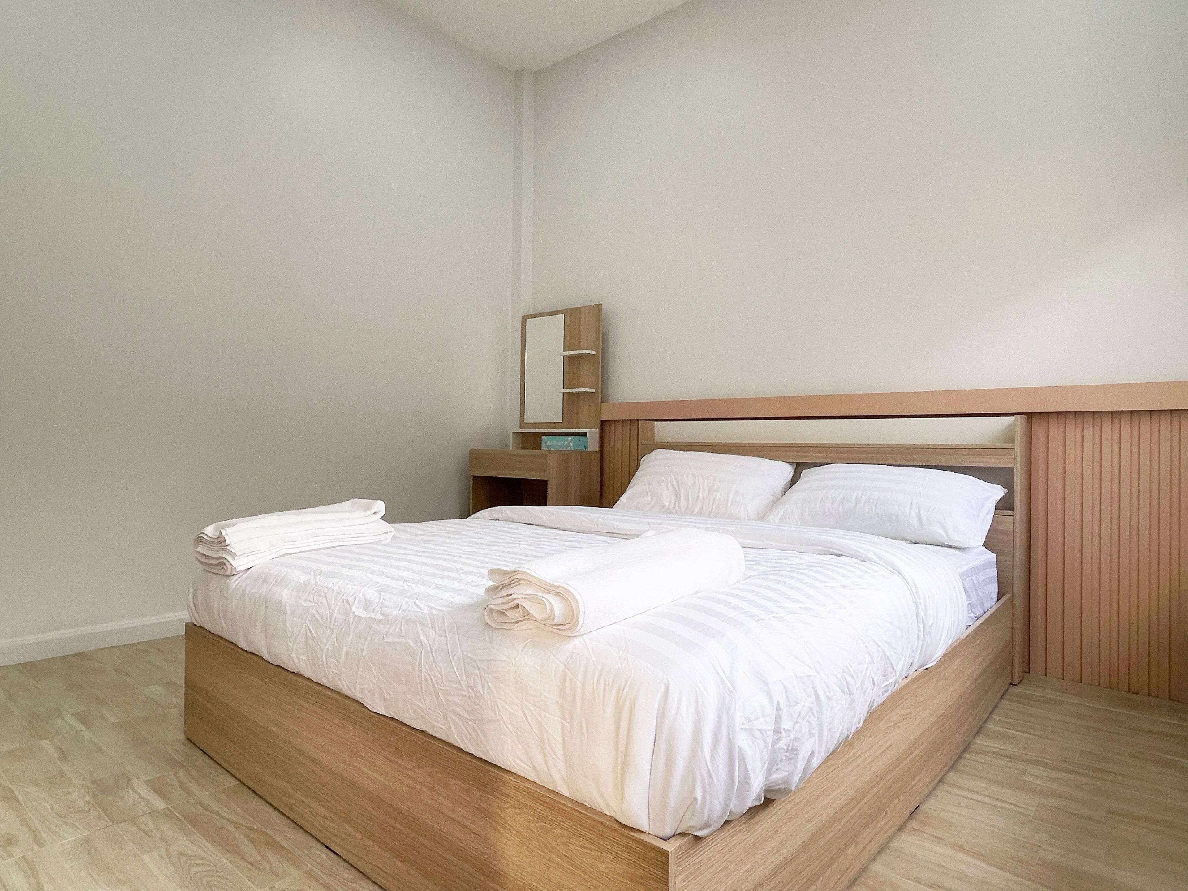 Una cama bien hecha con sábanas y toallas blancas, un cabecero de madera, una mesita de noche con espejo y una pared lisa.