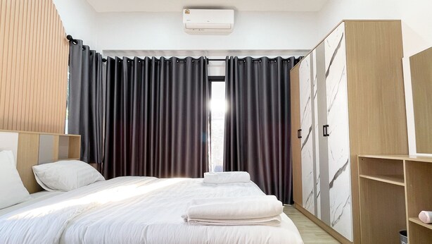 A modern hotel room with a large bed, a wardrobe, and a built-in air conditioning unit.