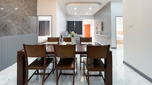 A modern dining area with a marble floor, wooden chairs, a chandelier, and a television on the wall.