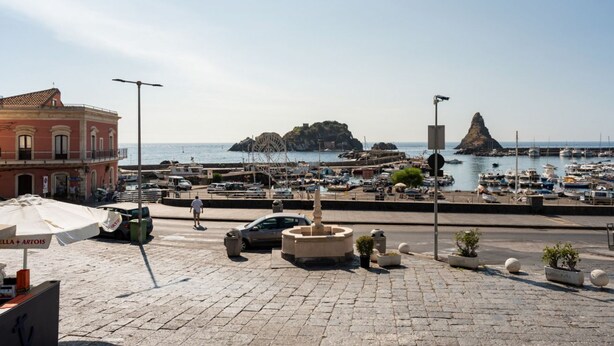 A coastal town with a marina, a fountain, and a red building with a sign.