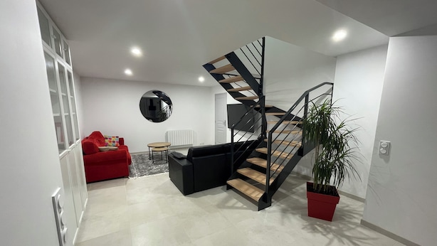 A modern living room with a staircase, a red sofa, a round mirror, and a potted plant. - Large Duplex Apartment 85m2 (Fleurieux-sur-l'Arbresle)