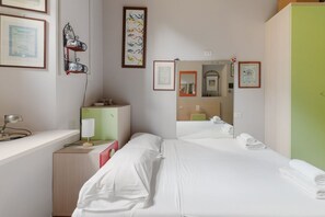 Ein Hotelzimmer mit einem Bett, einem Schreibtisch mit Lampe, einer Kommode, einem Spiegel und gerahmten Zertifikaten an der Wand.