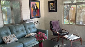 A living room with a green leather sofa, a black coffee table with a vase of flowers, a ceiling fan, and a view of the outdoors through a window. - Central pet-friendly private house located by U of A with pool and hot tub (Tucson)