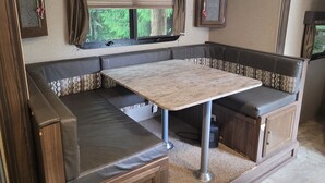 Ein kompaktes Wohnmobil-Interieur mit Essbereich, gepolsterten Sitzmöglichkeiten und einem Fenster mit Vorhängen.