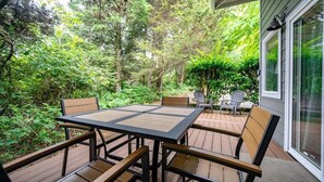 An outdoor patio with a table and chairs, surrounded by dense greenery and trees. - Beach Bungalow 4 - 700ft to Beach - Dogs Ok! (Cannon Beach)