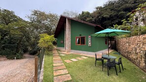 Una casa con fachada verde, un muro de piedra y un patio con mesa y sillas.