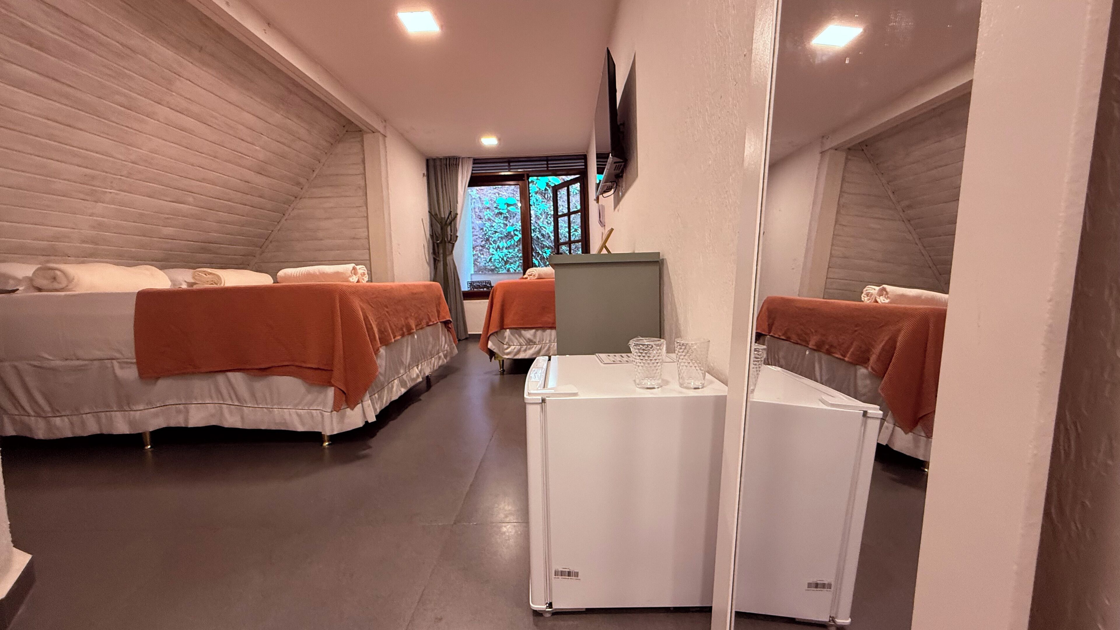 A hotel room with two beds, a small table with glasses, and a TV on the wall.