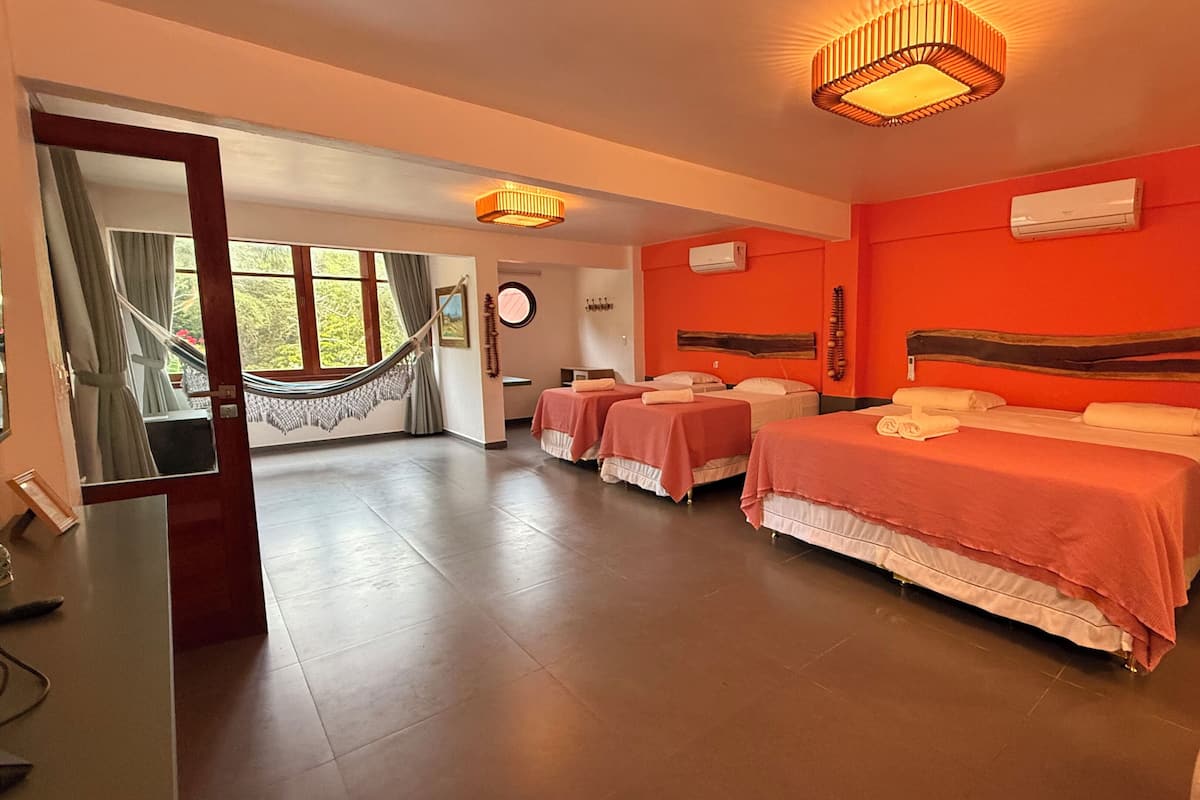 A hotel room with four beds, a hammock, and a large window.